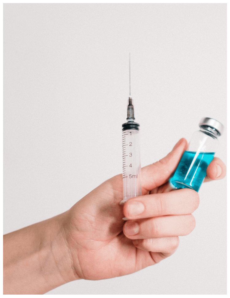 Hand holding syringe and vial of blue liquid.