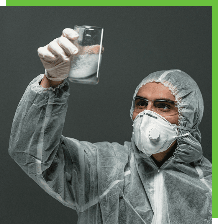 Scientist in protective gear examining liquid.